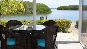 A dining area with wicker chairs and a glass table, overlooking a body of water and greenery. - Spoonbill Lagoon with Fantastic Water Views of Palma Sola Bay! (Bradenton)