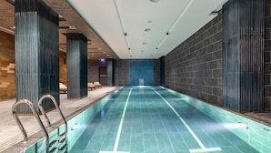 An indoor swimming pool with clear water, surrounded by dark tiled walls and a wooden bench area. - Wish More Hotel Şişli (Istanbul)