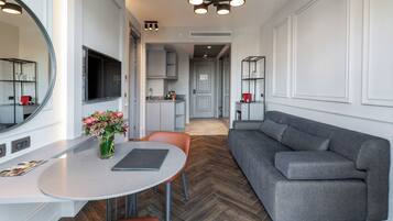 A modern living room with a grey sofa, a dining table with a vase of flowers, and a TV mounted on the wall.