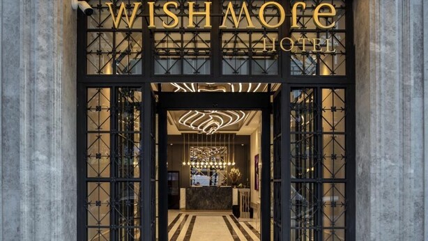 The entrance of the Wishmoe Hotel with a modern design, featuring a large illuminated sign above the entrance and a geometric patterned glass door. - Wish More Hotel Şişli (Istanbul)