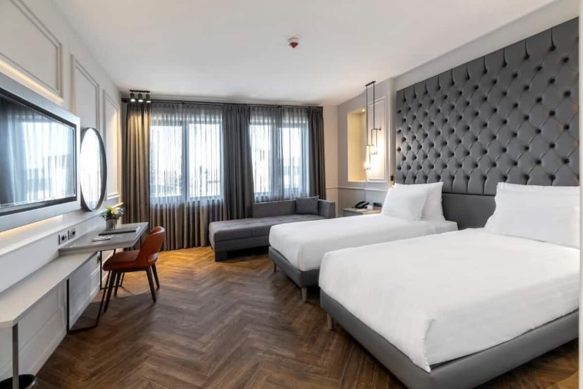 A hotel room with two beds, a desk, and a seating area.