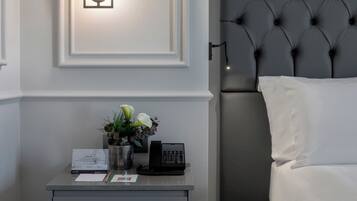 A hotel room with a neatly made bed, a bedside table with a telephone, a vase with flowers, and a framed picture on the wall.