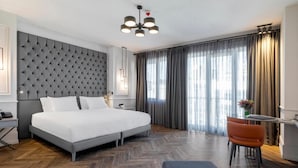 A modern hotel room with a tufted headboard, a large bed, a desk with a chair, and a view of the outdoors through large windows. - Wish More Hotel Şişli (Istanbul)