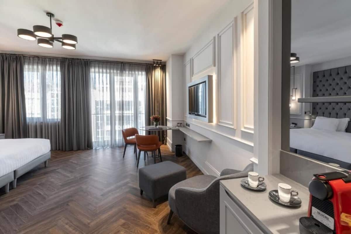 A hotel room with a large bed, a desk with a coffee maker, a TV, and a view of the city.