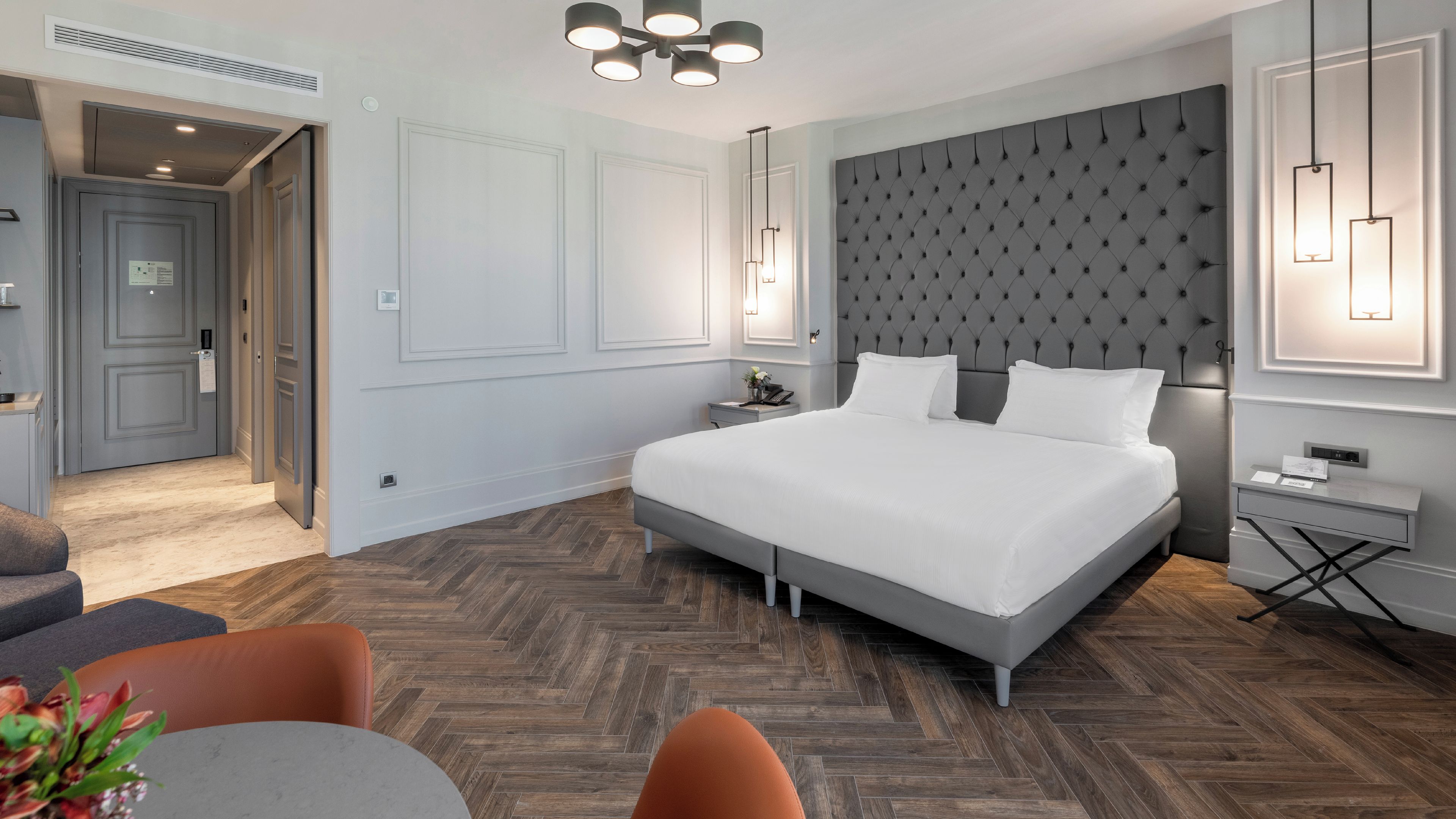 A modern hotel room with a large bed, a bedside table, a desk, and a chair.