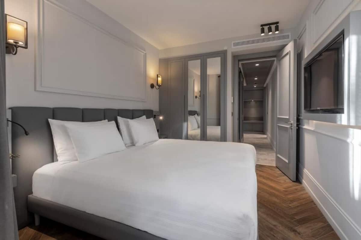 A modern hotel room with a large bed, a flat-screen TV, and a walk-in closet.