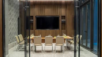 A modern conference room with a large flat-screen TV, glass walls, and a wooden panel wall.