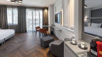A hotel room with a bed, a desk, a chair, a sofa, a TV, and a coffee machine.