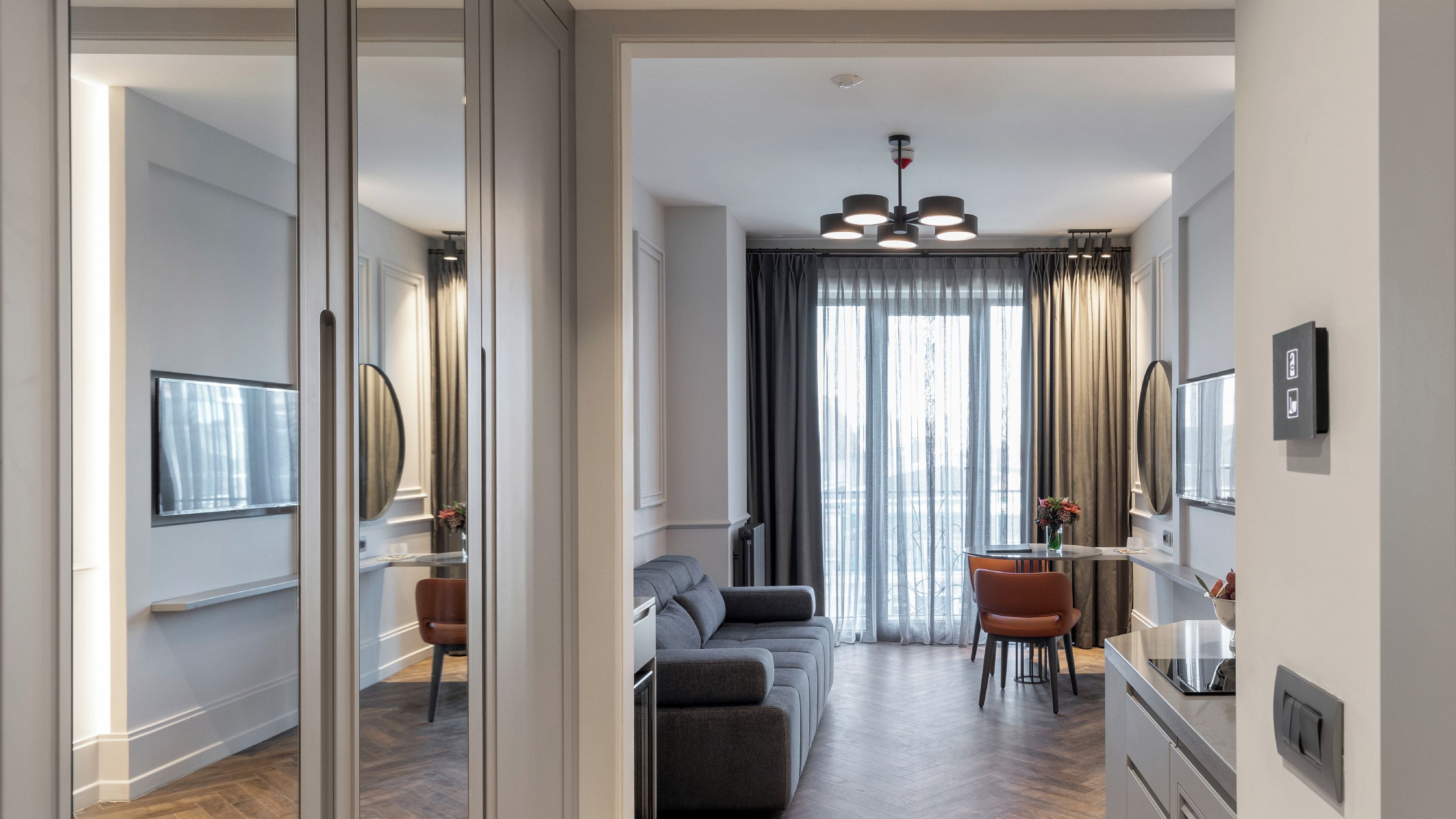 Une chambre d’hôtel moderne équipée d’un canapé, d’une table à manger, de chaises et d’une grande fenêtre avec des rideaux.
