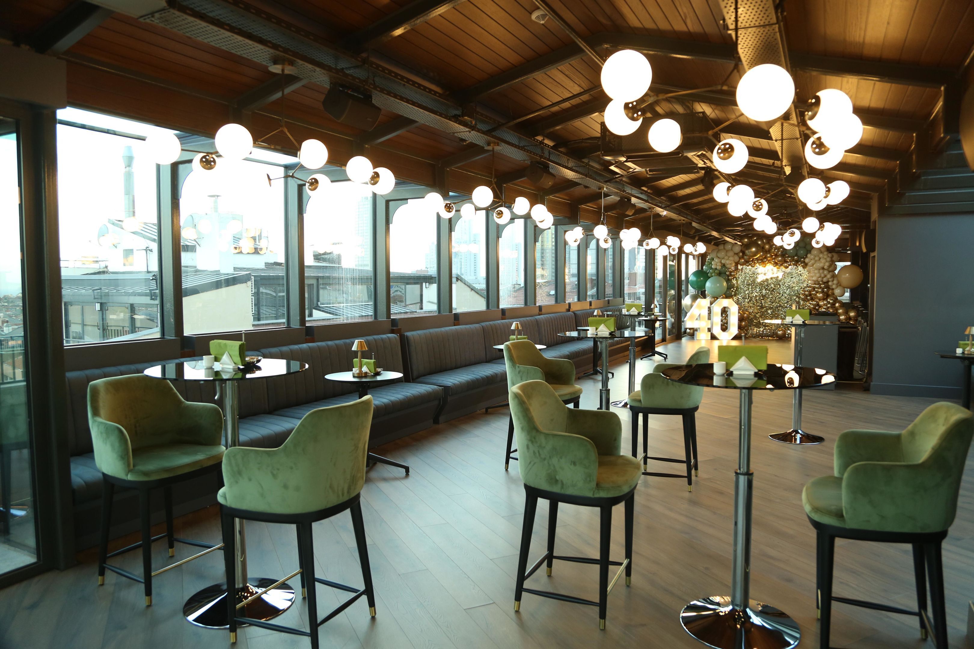 A modern interior with high ceilings, round tables, and green upholstered chairs.