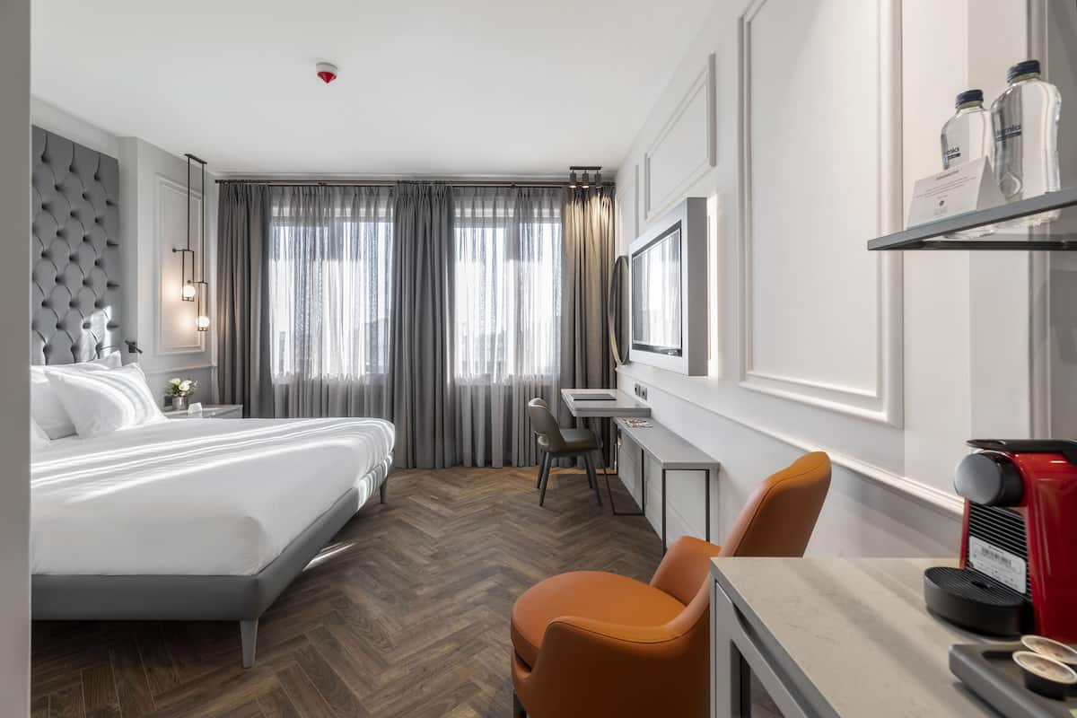 A modern hotel room with a large bed, a desk, and a coffee machine.