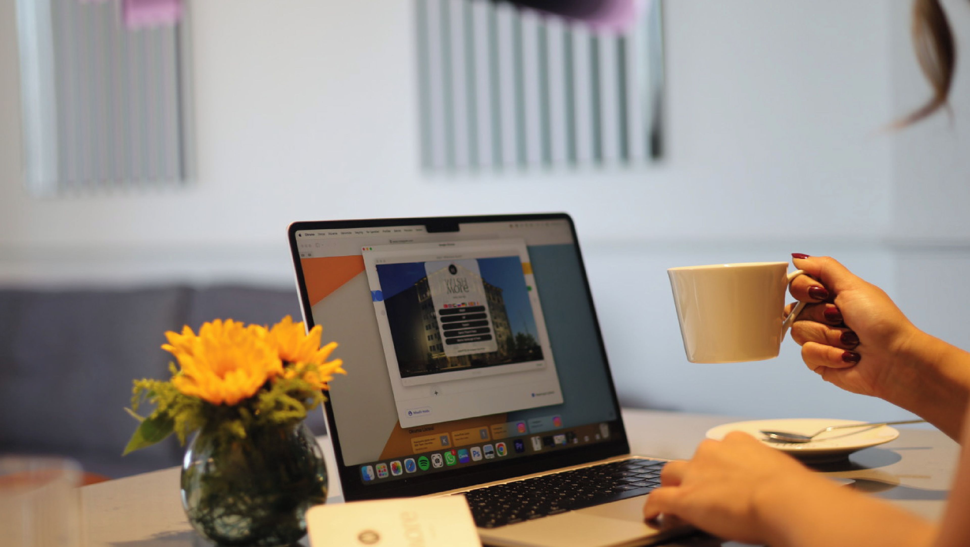 Un ordinateur portable sur une table, avec une tasse de café, un vase de fleurs et un téléphone intelligent.