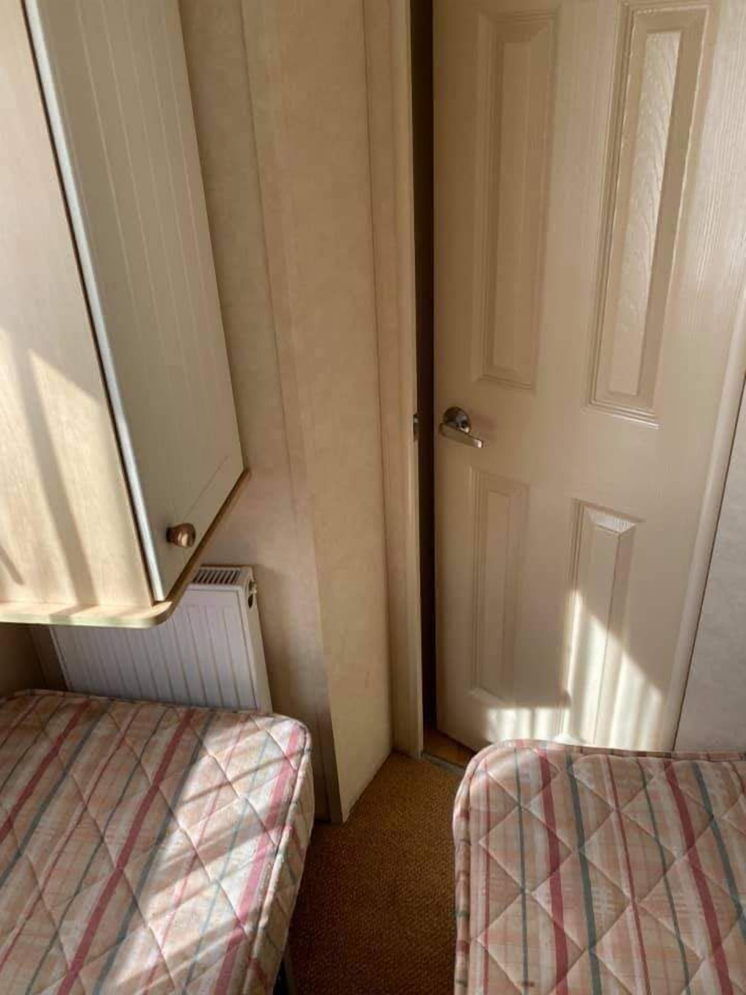 Et lille, smalt værelse med to senge, en radiator og en dør.