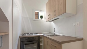 Eine kleine Küche mit Gasherd, Backofen und einem Fenster mit Pflanze.