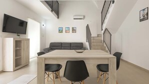 Ein modernes Wohnzimmer mit großem Fernseher, einer Couch, einem Esstisch mit Stühlen und einer Treppe.