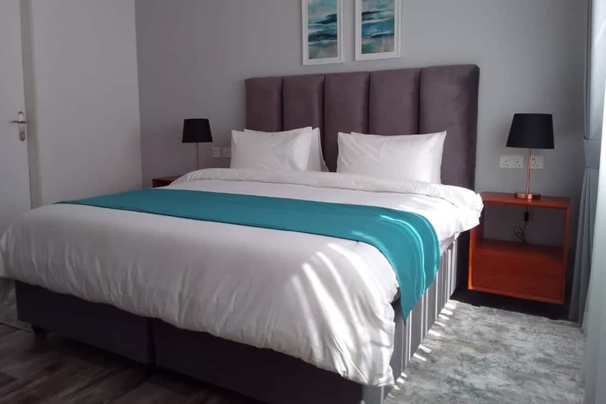 A bedroom with a large bed, two bedside tables, a nightstand, and two wall-mounted lamps.