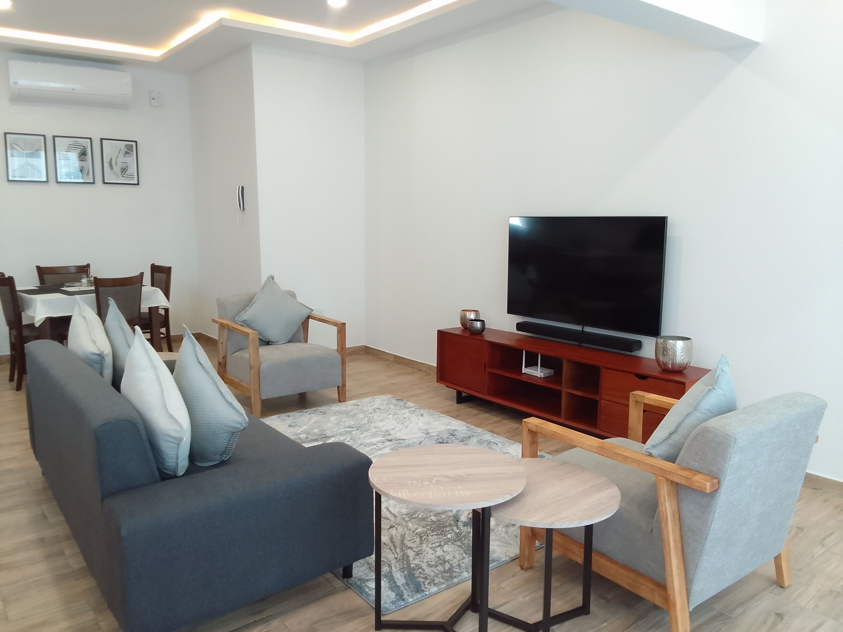 Una sala moderna con sofá, sillones, una mesa de centro, televisor y un comedor con sillas y una mesa.