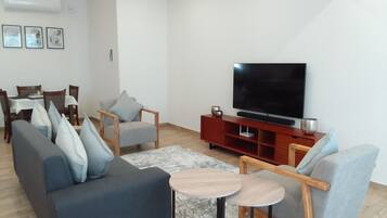 Una sala moderna con sofá, sillones, una mesa de centro, televisor y un comedor con sillas y una mesa.