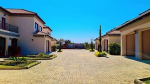 A courtyard with a paved walkway, surrounded by buildings with tiled roofs and balconies. - 24 Roma (Lusaka)