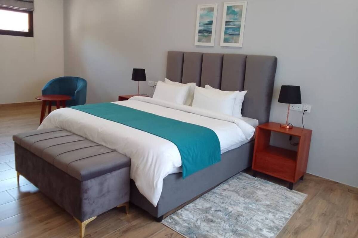 A modern bedroom with a large bed, a bench, two nightstands, and a window.
