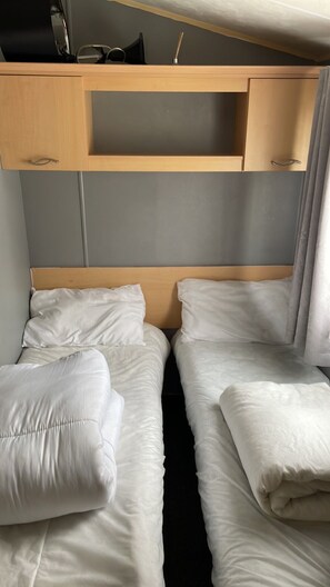 A twin room with two beds, a wooden headboard, a shelf above the beds, and a curtain on the right side. - Inviting 3-bed Caravan in Skegness (Skegness)