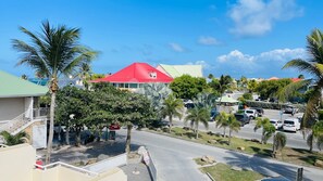 A street view with a red-roofed building, palm trees, and parked cars.