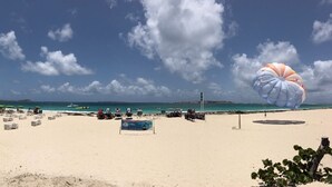 A beach with a parasail, beach chairs, and a small building.