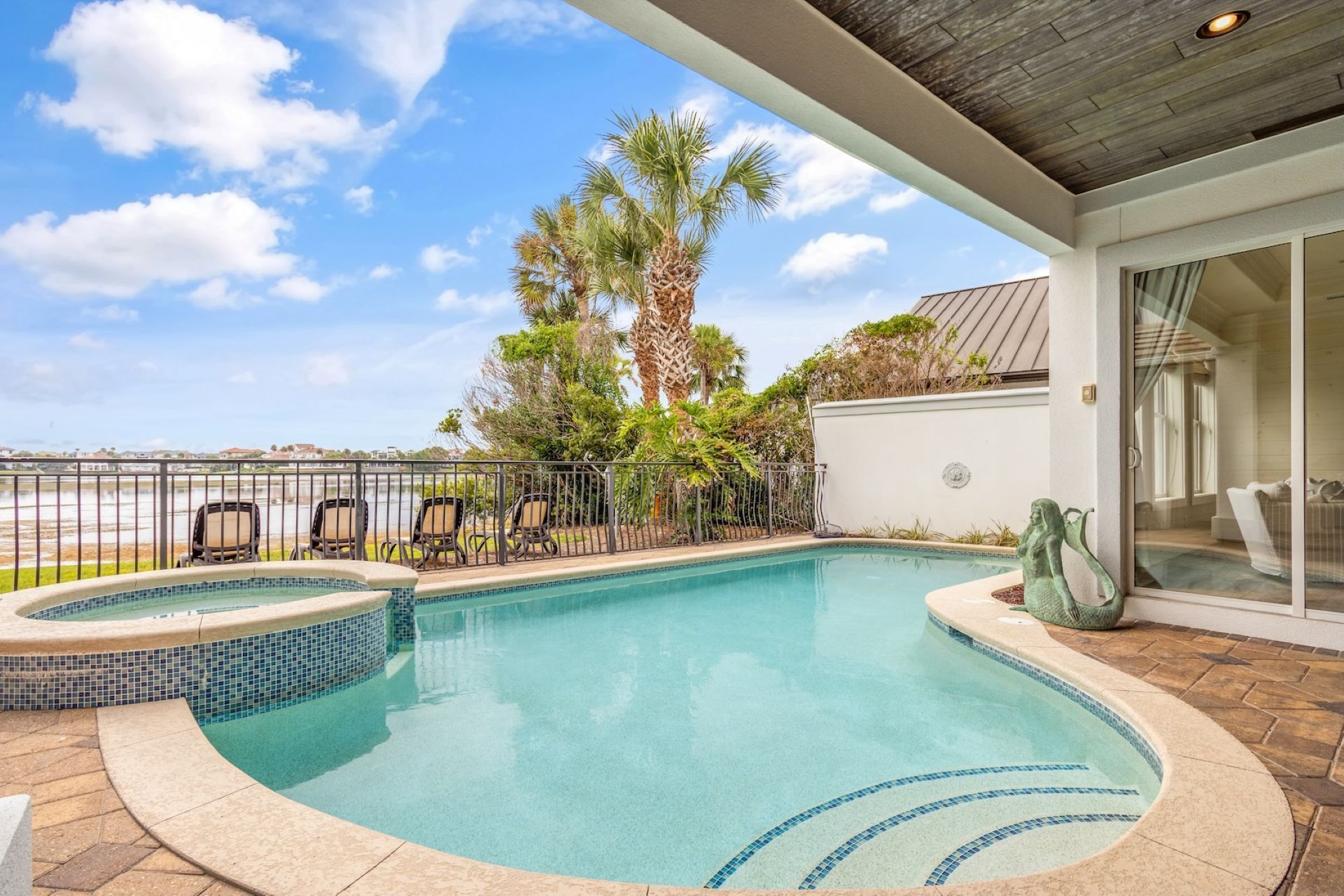 A swimming pool with a hot tub, surrounded by lounge chairs, palm trees, and a view of the water.
