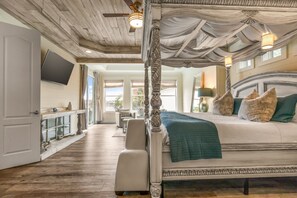 A spacious bedroom with a four-poster bed, a large window, and a wooden ceiling.