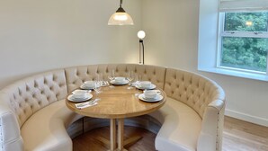 A round dining table with white plates and glasses, surrounded by a beige upholstered bench. - The Old Schoolhouse - Character Stay on NC500 (Tongue)