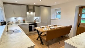 A modern kitchen with white cabinets, a built-in oven, and a dining area with a wooden table set for four. - The Old Schoolhouse - Character Stay on NC500 (Tongue)