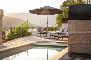 A poolside area with a lounge chair, umbrella, and a stone wall. - Feel Discovery Casa de Cima (Baiao)