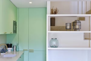 Una cocina moderna con armarios color turquesa, una encimera blanca y una unidad de estanterías blanca con objetos decorativos.