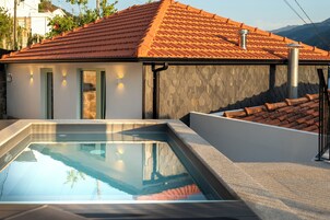 A modern building with a swimming pool, stone walls, and a tiled roof.