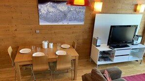 Een gezellige kamer met een houten eettafel gedekt voor vier personen, een flatscreen televisie en een comfortabele bank.