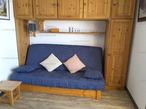 A blue sofa with cushions, wooden cabinets, and a small table in a room. - Paradiski closed to the slopes and shops vallandry (LANDRY)