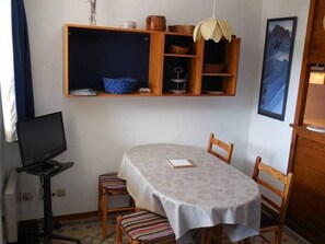 Ein kleiner Essbereich mit einem runden Tisch, zwei Stühlen, einem Fernseher und einem Regal mit diversen Gegenständen.