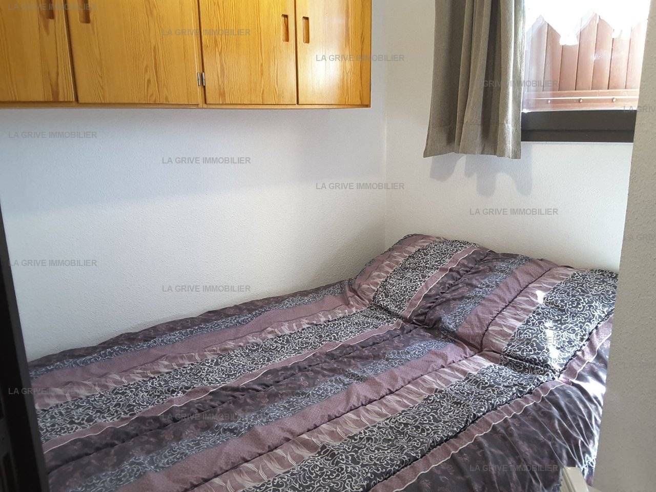A small bedroom with a single bed, a wooden wardrobe, and a window with curtains.