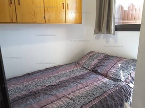 Une petite chambre à coucher avec un lit simple, une armoire en bois et une fenêtre avec des rideaux.