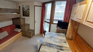 A compact room with a bunk bed, a red sofa, a small table, and a television.