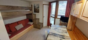 Habitación pequeña con una litera, un sofá rojo, una mesita y un televisor.