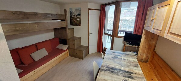 Habitación pequeña con una litera, un sofá rojo, una mesita y un televisor.