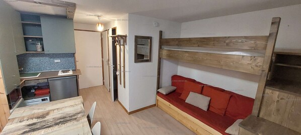 Habitación compacta con kitchenette, una litera con ropa de cama roja y una pequeña zona de estar.