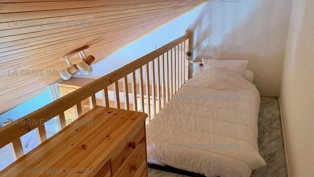 Une chambre avec un lit superposé en bois et un lit simple, une rambarde en bois et un ventilateur de plafond.
