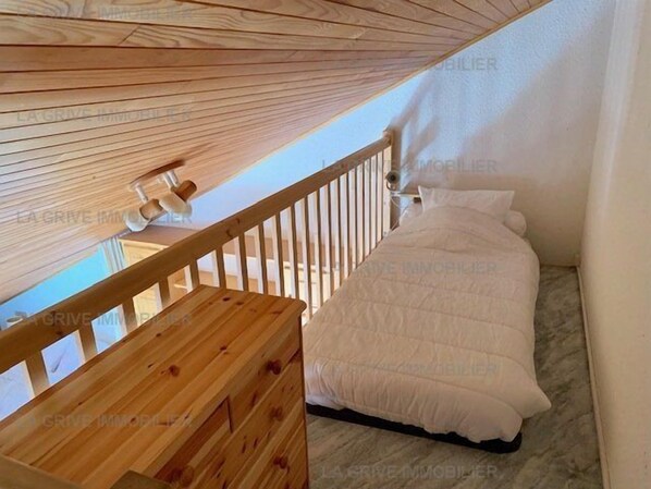 A bedroom with a wooden bunk bed and a single bed, a wooden railing, and a ceiling fan.