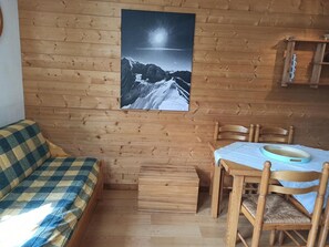 A wooden interior with a sofa, a dining table with chairs, and a small cabinet.