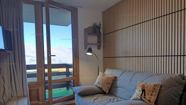 A living room with a sofa, a lamp, a television, and a view through a glass door. - Paradiski closed to the slopes vallandry (LANDRY)