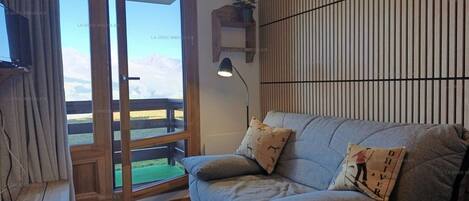 Una sala de estar con un sofá, una lámpara, un televisor y vistas a través de un ventanal.