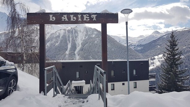 Ein verschneiter Eingangsbereich mit einem Schild, auf dem 'BALIET' steht, und einem Gebäude im Hintergrund.