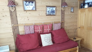 Ein Bett mit Holzrahmen, roter Bettwäsche und herzförmigen Kissen, ein kleiner Nachttisch und eine Lampe.